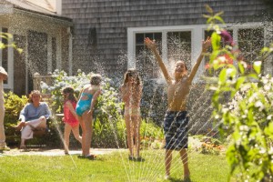 Group of four children playing around a sprinkler in a garden